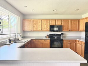 A modern kitchen with wooden cabinets, a stainless steel sink, a microwave, an oven, and a refrigerator.