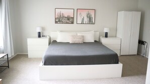 A bedroom with a large bed, white nightstands, two wall-mounted lamps, a white wardrobe, and two framed desert plant pictures. - Spacious & Spotless Family Retreat -Single-Story Comfort – Close to Everything! (Mesa)
