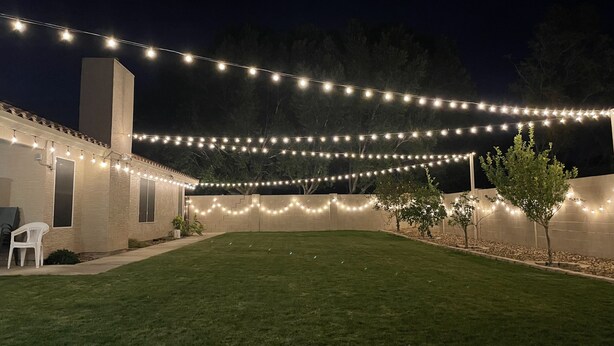 A backyard with a lawn, string lights, a white chair, and a small tree. - Spacious & Spotless Family Retreat -Single-Story Comfort – Close to Everything! (Mesa)