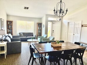 A spacious living room with a dining area, a chandelier, and a bookshelf.