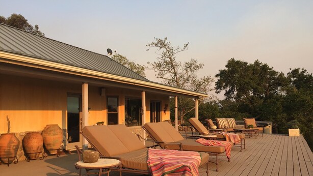 A wooden deck with lounge chairs and a table, a building with a metal roof, and large pots against the wall. - Dragonfly Ranch-Stunning Ocean View 320 Acre Ranch (Atascadero)
