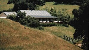 A house with a sloped roof, surrounded by a grassy hill and trees. - Dragonfly Ranch-Stunning Ocean View 320 Acre Ranch (Atascadero)