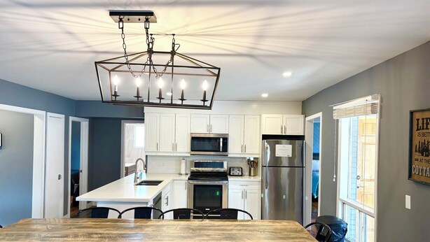 A modern kitchen with white cabinets, stainless steel appliances, and a wooden dining table. - Mountain View 4BR Chalet with contactless entry - The Lake at Blue Mountains (Blue Mountains)