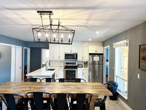 A modern kitchen with white cabinets, stainless steel appliances, and a wooden dining table. - Mountain View 4BR Chalet with contactless entry - The Lake at Blue Mountains (Blue Mountains)