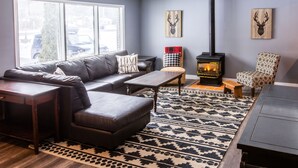 A living room with a black leather sofa, a patterned rug, a fireplace, and two deer head wall art pieces. - Mountain View 4BR Chalet with contactless entry - The Lake at Blue Mountains (Blue Mountains)