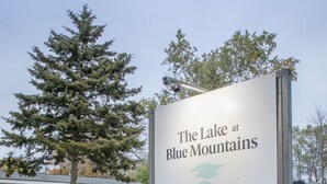 A sign for 'The Lake at Blue Mountains' with a view of a building and a large tree in the background. - Mountain View 4BR Chalet with contactless entry - The Lake at Blue Mountains (Blue Mountains)