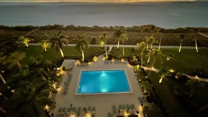 Un complexe hôtelier doté d’une piscine, de palmiers et offrant une vue sur l’océan au coucher du soleil.