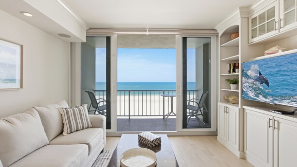 Un salon avec un canapé, une table basse et un téléviseur. On peut admirer la plage à travers une porte vitrée.