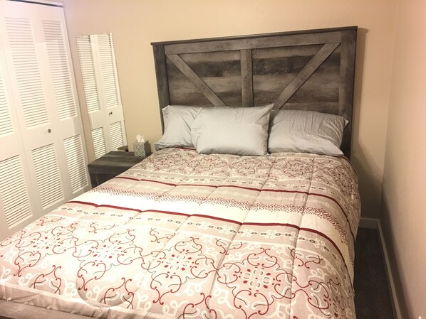 Un dormitorio con cama, mesita de noche y puerta con contraventanas.