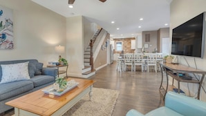 A modern living room with a sofa, coffee table, and TV. There is a staircase leading to a kitchen area with a dining table and chairs. - 22 Grover's Ocean, spacious 5 bedroom home with central AC, 1 block to beach! (Ocean Grove)