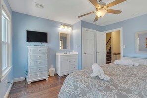 Cozy retreat with a large bed, flat-screen TV, and ceiling fan, set against a light blue backdrop.