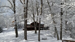 Una cabaña de madera rodeada de árboles nevados, una valla de madera y una mesa de picnic en un paisaje cubierto de nieve.