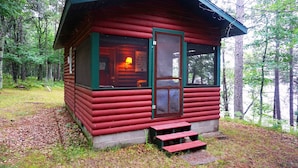 En hyggelig hytte med rødt ydre, en dør og et vindue med et lys i.