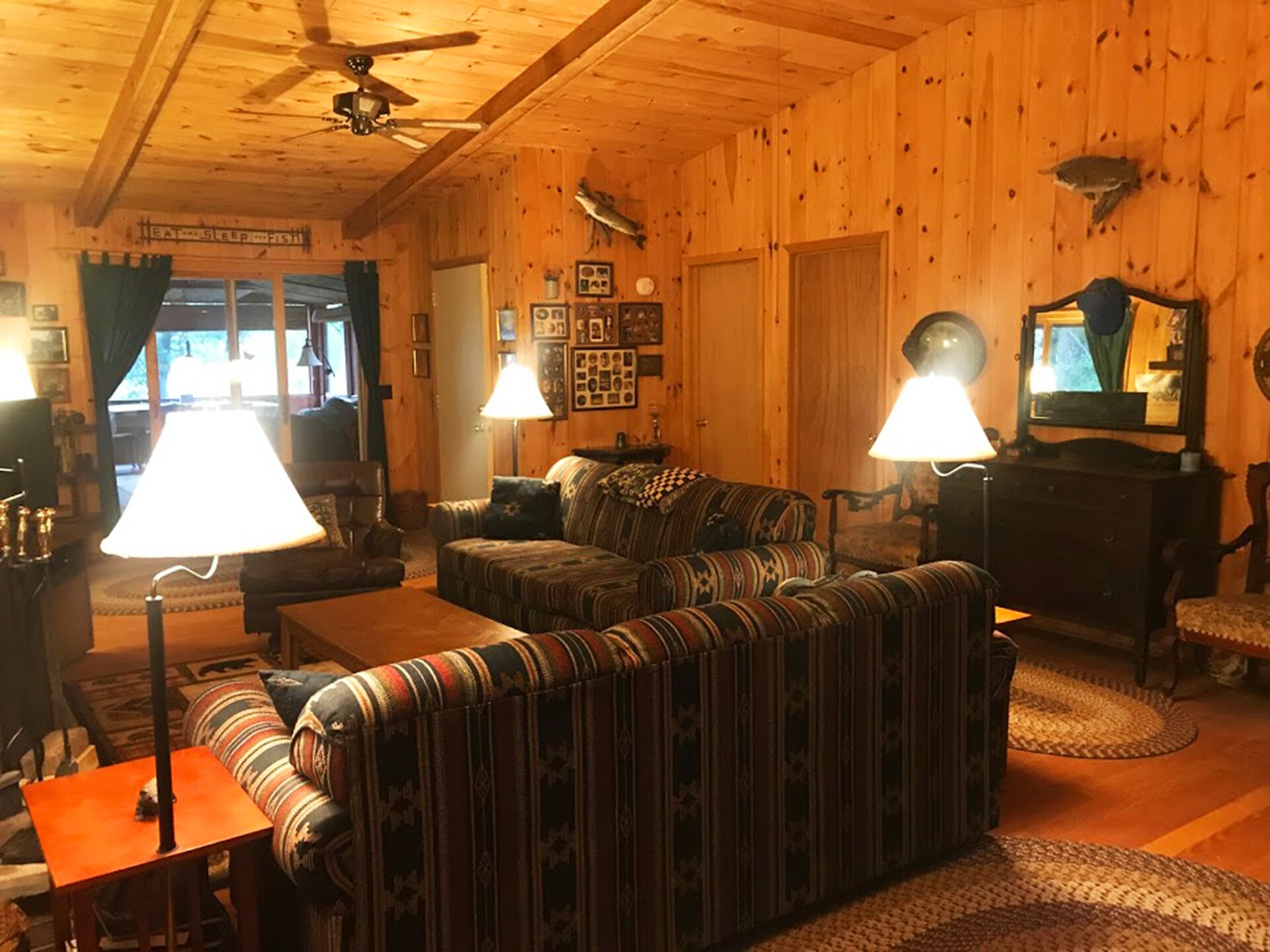 A cozy wooden cabin interior with a sofa, armchairs, a table, and a ceiling fan.
