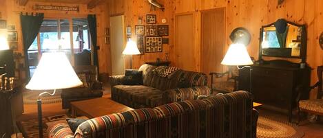 A cozy wooden cabin interior with a sofa, armchairs, a table, and a ceiling fan.