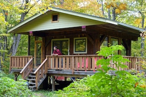 Surrounded by lush greenery, this cabin features a wooden deck and a staircase leading to the entrance.