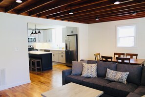 A modern kitchen with a refrigerator, microwave, and island. There is a dining area with a table and chairs. The room has wooden flooring and a ceiling with exposed beams. - Back Your Boat Into Center Hill Lake From Our Home!  Swim, Fish, Hunt, Relax! (Baxter)