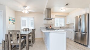 Une cuisine moderne avec des meubles blancs, un réfrigérateur en acier inoxydable et un coin repas comprenant des chaises et une table en bois.