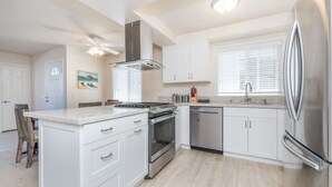 Une cuisine moderne avec des meubles blancs, des appareils en acier inoxydable et une table à manger en bois.