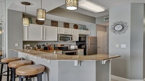 A modern kitchen with white cabinets, a large island with stools, a microwave, oven, and refrigerator. - Luxury at it's finest! Penthouse unit overlooking the beautiful Gulf of Mexico! (Fort Walton Beach)