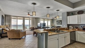 A spacious living area with a large window overlooking the ocean, a kitchen with white cabinets, and a dining area with a table and chairs. - Luxury at it's finest! Penthouse unit overlooking the beautiful Gulf of Mexico! (Fort Walton Beach)