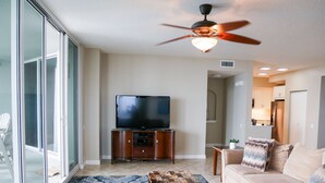 A living room with a flat-screen TV, wooden entertainment center, and a ceiling fan. - Beach Colony West 3C/Gulf Front 3BR/3BA w/Beach Chair Service & WINTER RATES (Navarre Beach)