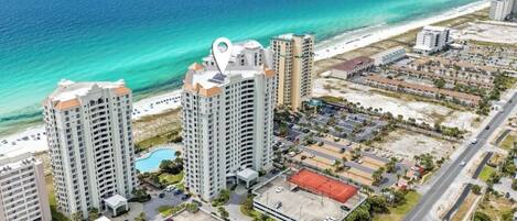 A high-rise hotel with multiple floors, a swimming pool, and a tennis court.