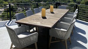 A terrace with a wooden table and wicker chairs, overlooking a scenic landscape. - Hilltop 365: Downtown Luxury ~ Stunning Views ~ Hilltop ~ 3 Blocks To Downtown  (Paso Robles)
