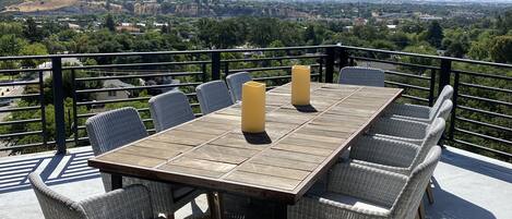 Una terraza con mesa de madera y sillas de mimbre, con vistas a un paisaje pintoresco.