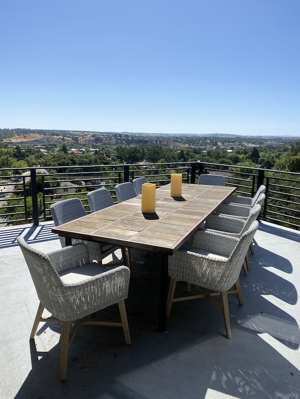 Una terraza con mesa de madera y sillas de mimbre, con vistas a un paisaje pintoresco.
