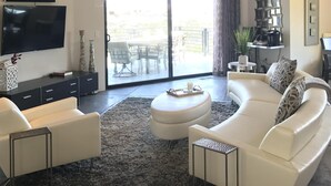 A modern living room with a large sectional sofa, a flat-screen TV, and a dining area with a table and chairs. - Hilltop 365: Downtown Luxury ~ Stunning Views ~ Hilltop ~ 3 Blocks To Downtown  (Paso Robles)