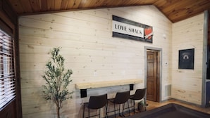 Una habitación acogedora con una pared de madera, un banco, tres sillas, una planta en maceta y un letrero que dice 'LOVE SHACK'.