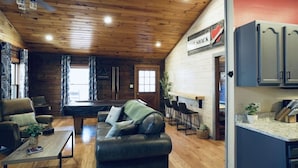Interior acogedor de una cabaña con mesa de billar, sofá de cuero y un letrero que dice 'LOVE SHACK'.