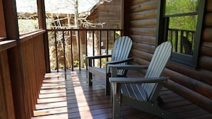 Una terraza de madera con sillas Adirondack y un banco, con vistas a un área boscosa.