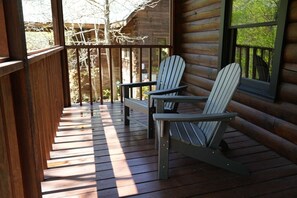 Une terrasse en bois, agrémentée de chaises Adirondack et d’un banc, donnant sur une zone boisée.