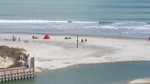 Una spiaggia con un molo di legno, una tenda rossa e persone che si rilassano sulla sabbia.