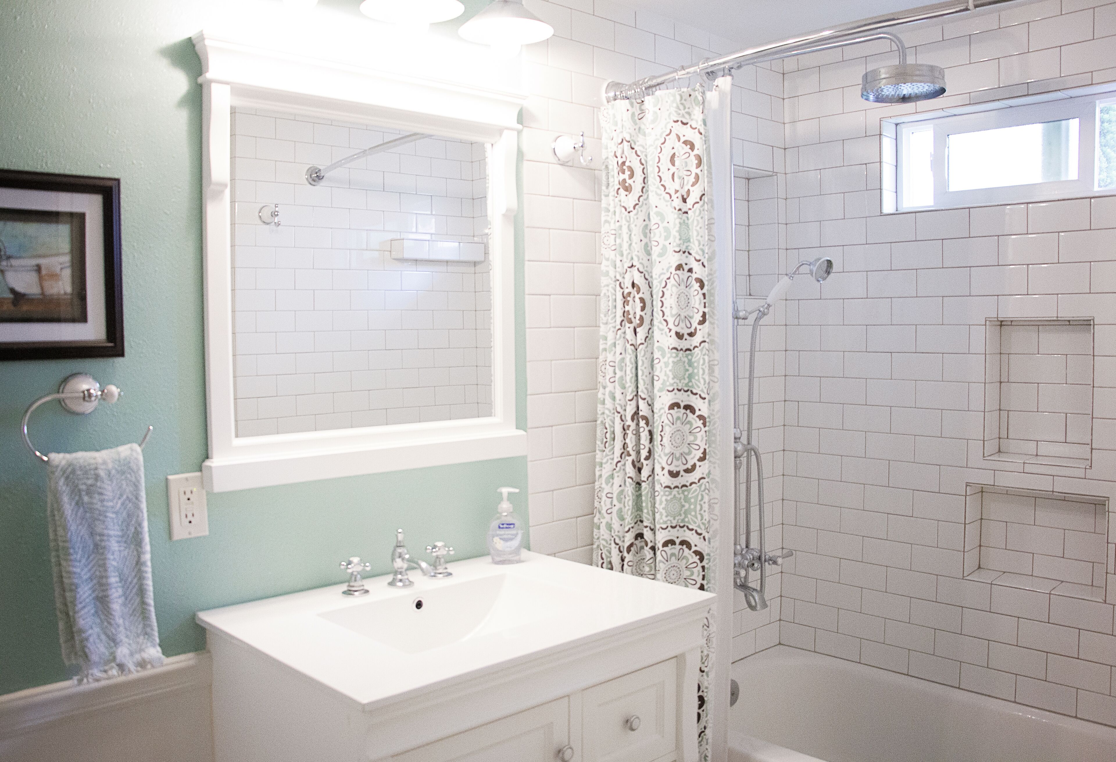 Un baño con un lavabo blanco, un espejo, una ducha con puerta de cristal y una cortina de ducha estampada.