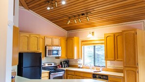 Eine Küche mit Holzausstattung, einem schwarzen Kühlschrank, einer Mikrowelle und einem Herd. Zwei Holzsessel und eine weiße Kücheninsel mit Spüle sind ebenfalls vorhanden.