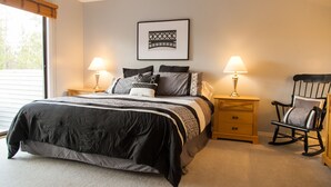Ein Schlafzimmer mit einem Bett, zwei Nachttischen, einem Schaukelstuhl und einem gerahmten Bild an der Wand.