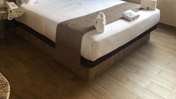 Quarto de hotel com cama grande, telefone ao lado da cama e cabeceira de madeira.