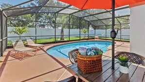 A covered outdoor area with a pool, lounge chairs, and a table with towels and a basket. - BUENAVENTURA LAKES (263HS) - 3BR 2BA home with pool in a private setting (Kissimmee)
