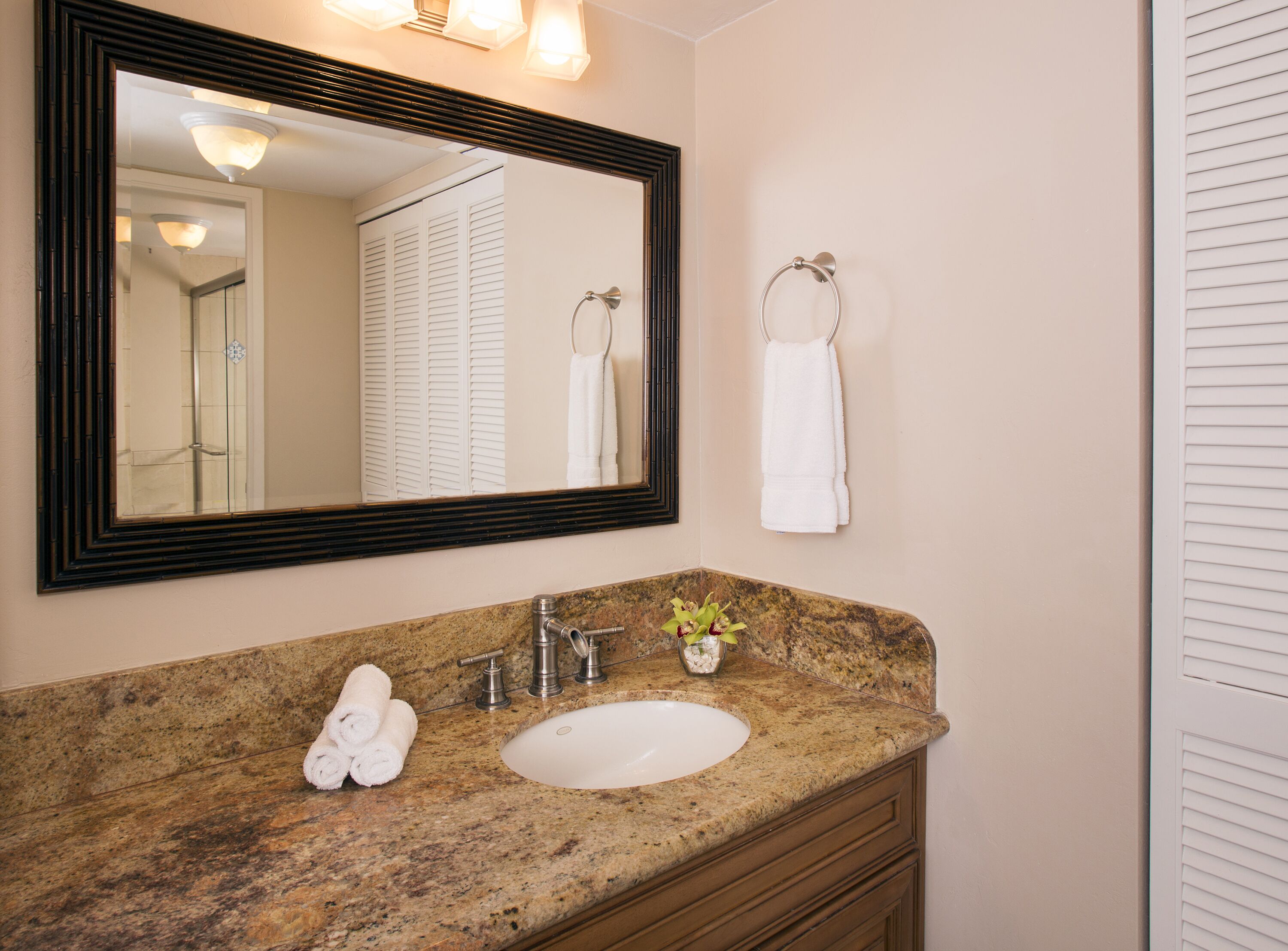 A bathroom with a granite countertop, a white sink, a mirror, and a towel rack.