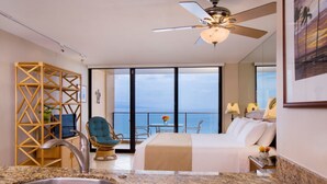 A hotel room with a bed, a sink, a balcony with a view of the ocean, and a ceiling fan.
