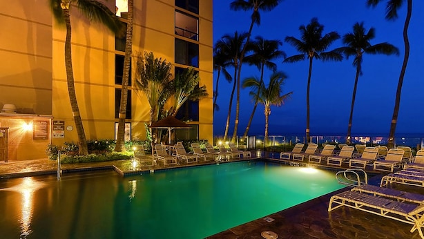 A pool area with lounge chairs, palm trees, and a building with a sign indicating no diving.