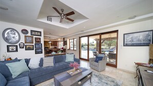 A spacious living room with a large sofa, coffee table, and a ceiling fan. There are framed pictures on the walls and a view of the backyard through large sliding doors. - Phoenix Scottsdale Golf House. NEW! Private Pickle Ball court. Great location. (Phoenix)