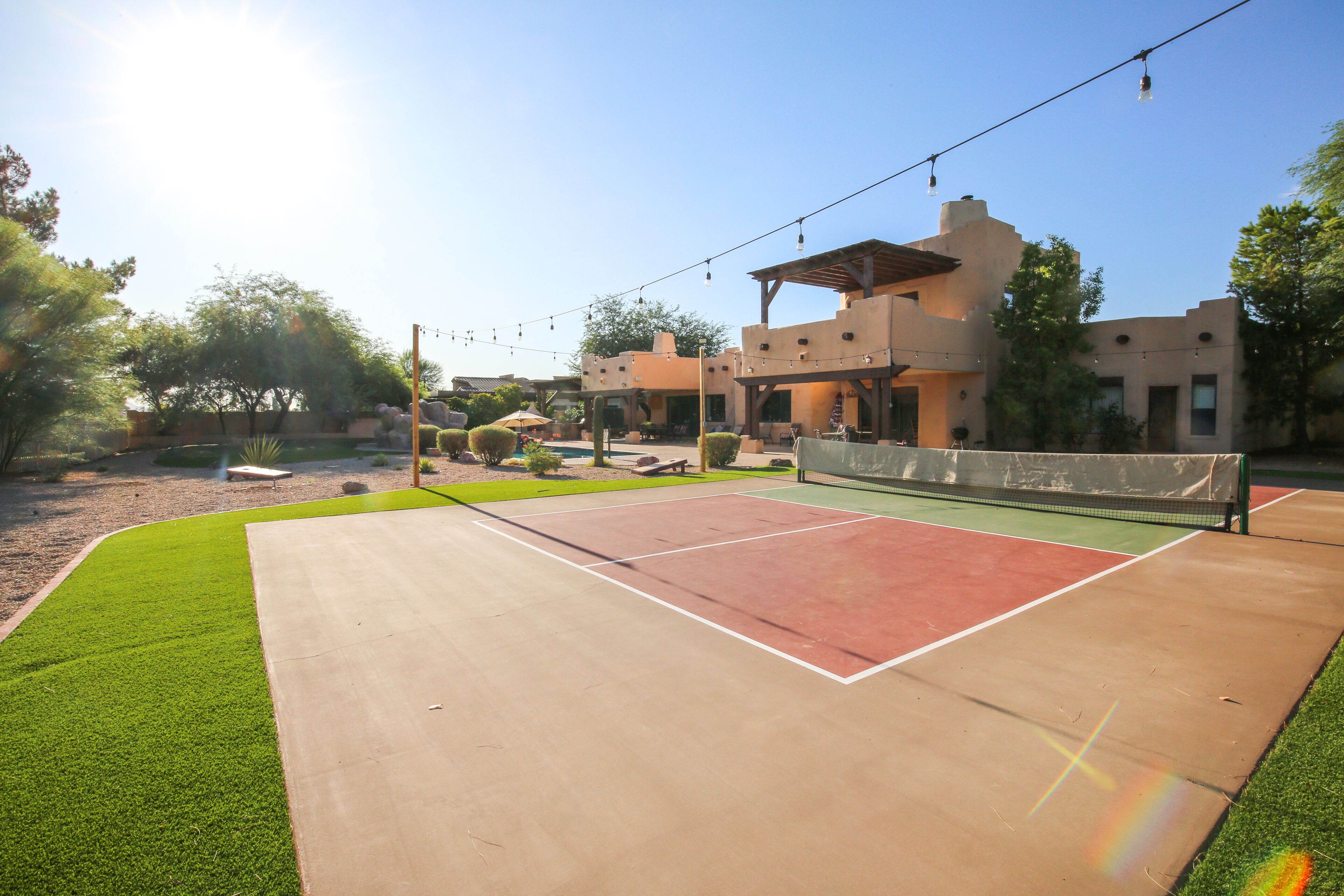 An outdoor tennis court with a net, surrounded by a landscaped area with trees and a building in the background.