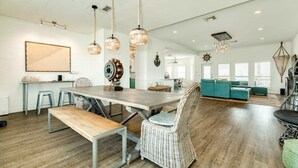 A spacious living area with a large wooden dining table, wicker chairs, and a teal sofa. - Captain's Quarters - Cabana, Hot Tub, Fire Pit, Fenced Yard! (Freeport)