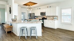 A spacious kitchen with white cabinetry, a central island with stools, and a large window providing natural light. - Captain's Quarters - Cabana, Hot Tub, Fire Pit, Fenced Yard! (Freeport)