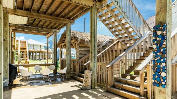 A covered outdoor area with a wooden staircase, white chairs, and a thatched roof structure. - Captain's Quarters - Cabana, Hot Tub, Fire Pit, Fenced Yard! (Freeport)