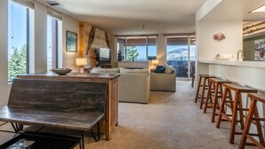 Un salon moderne comprenant un canapé, une table à manger avec des chaises, une cheminée et de grandes fenêtres donnant sur l’extérieur.